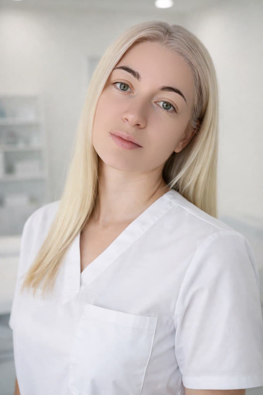 Professional portrait of Karina Gedarevych, Licensed Esthetician, wearing white uniform in clinical spa setting at Esthetics Elegance Lab